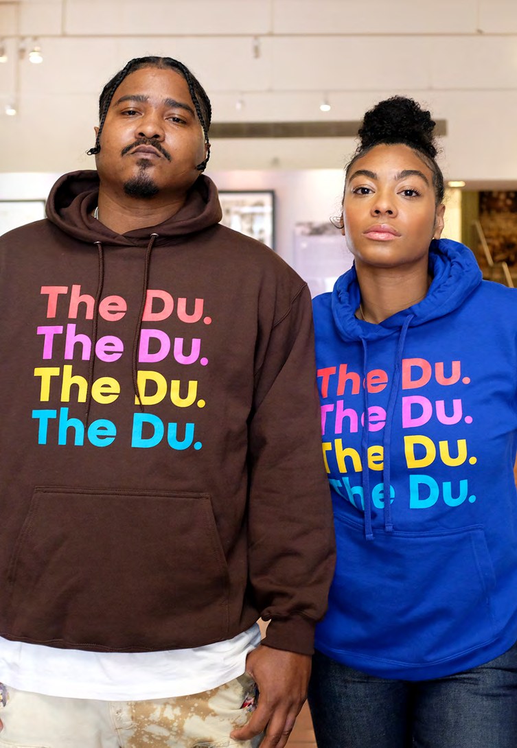 Two people wearing The Du. hoodies in the museum shop