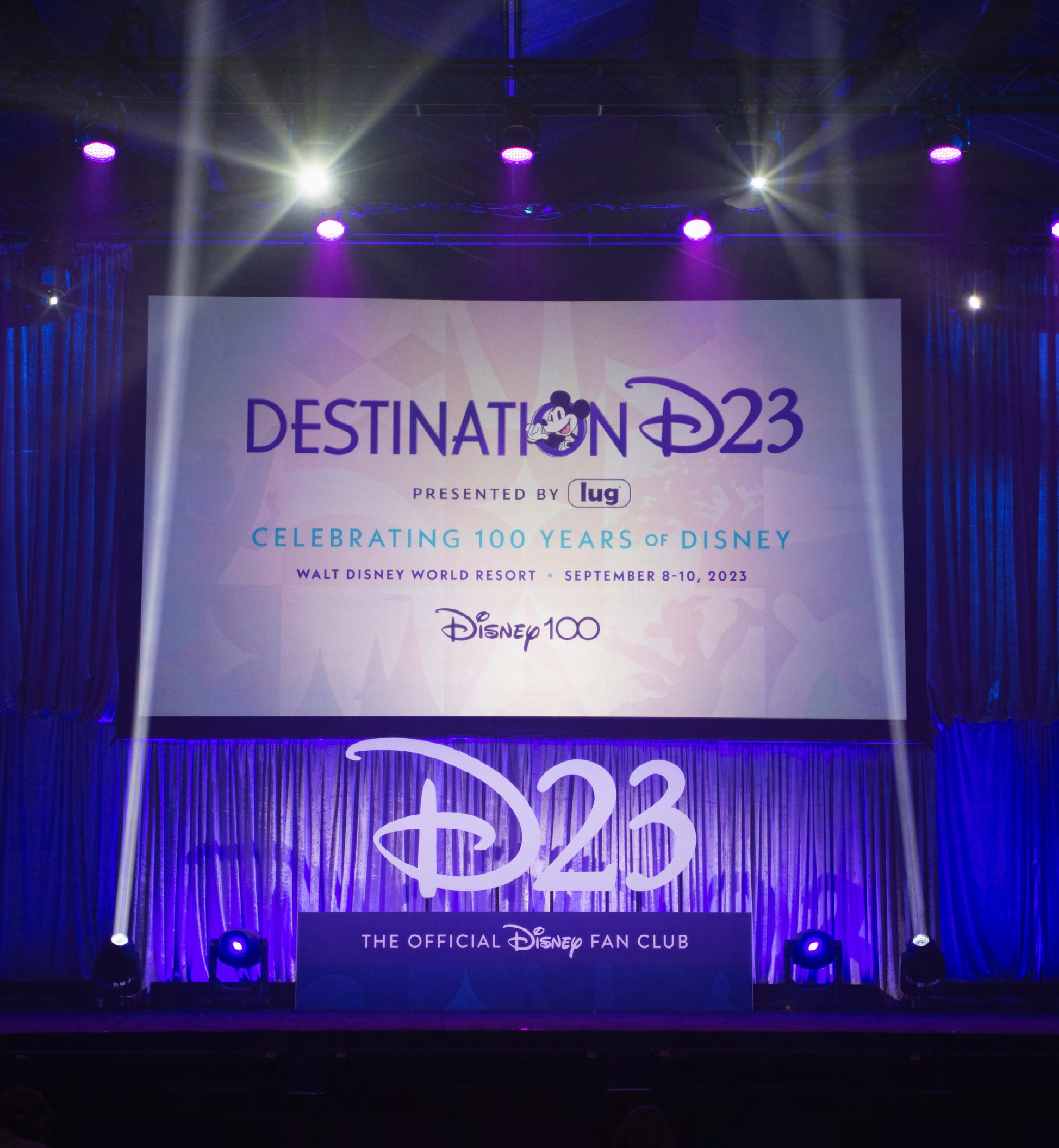 Destination D23 environmental and stage design for the Disney100 celebration, including custom character illustrations in Disney100 purple